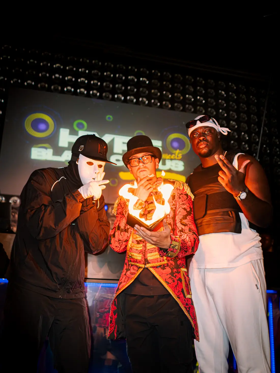 Three performers pose in front of the Hype screen, one holding a burning heart