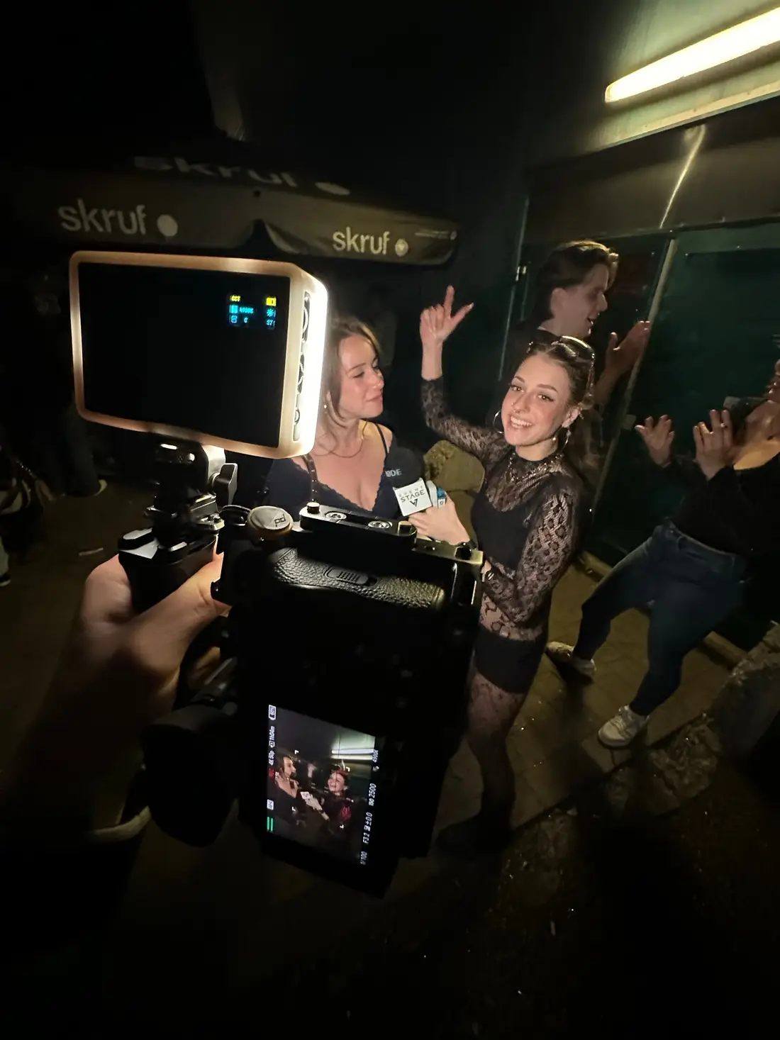 Camera with monitor and video light filming partying guests at Eventstage