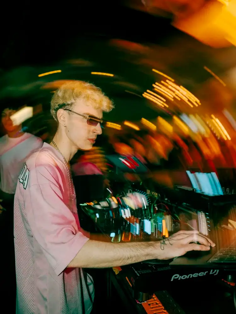 DJ in sunglasses at the decks, surrounded by light trails from a long exposure