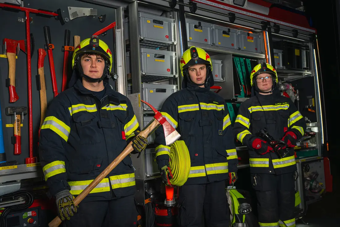 Drei Feuerwehrleute in Einsatzkleidung vor dem Geräteraum eines Löschfahrzeugs
