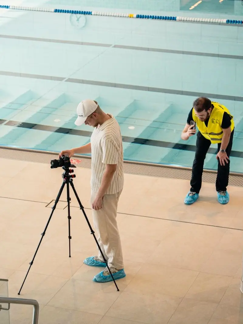 Photographer setting up the camera on a tripod by the sports pool at Bad Mirador, a staff member in a high-visibility vest next to him