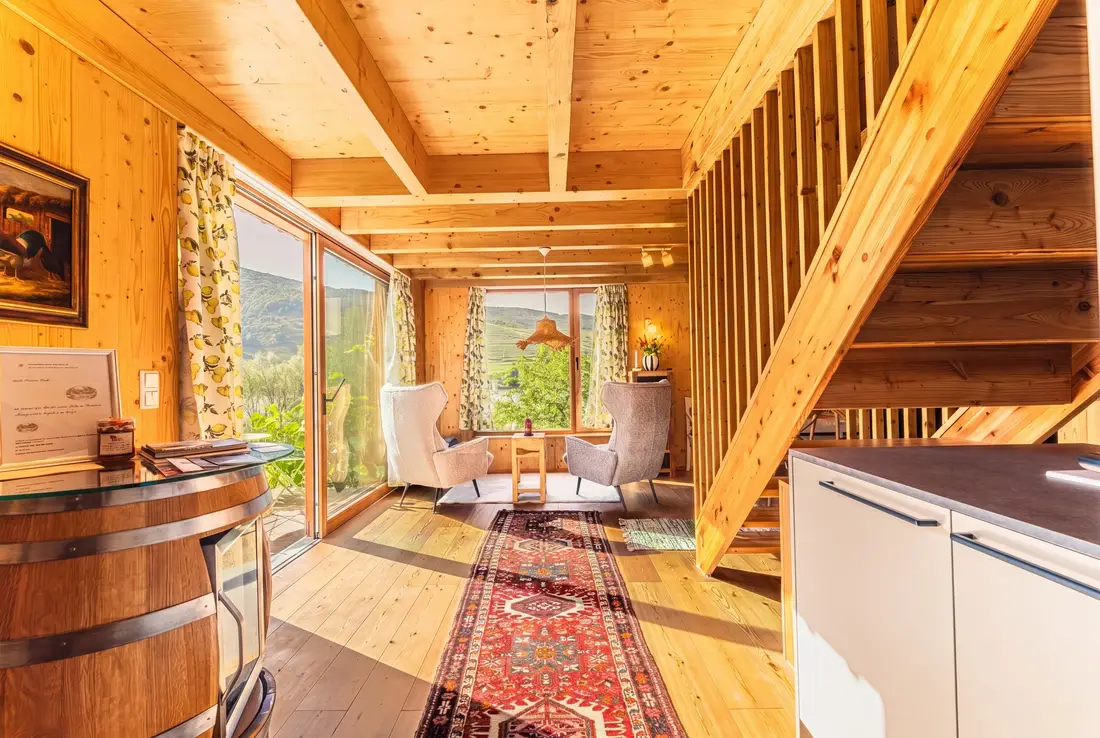 Wohnraum eines Holzhauses mit Treppe, Sitzecke und großen Fenstern