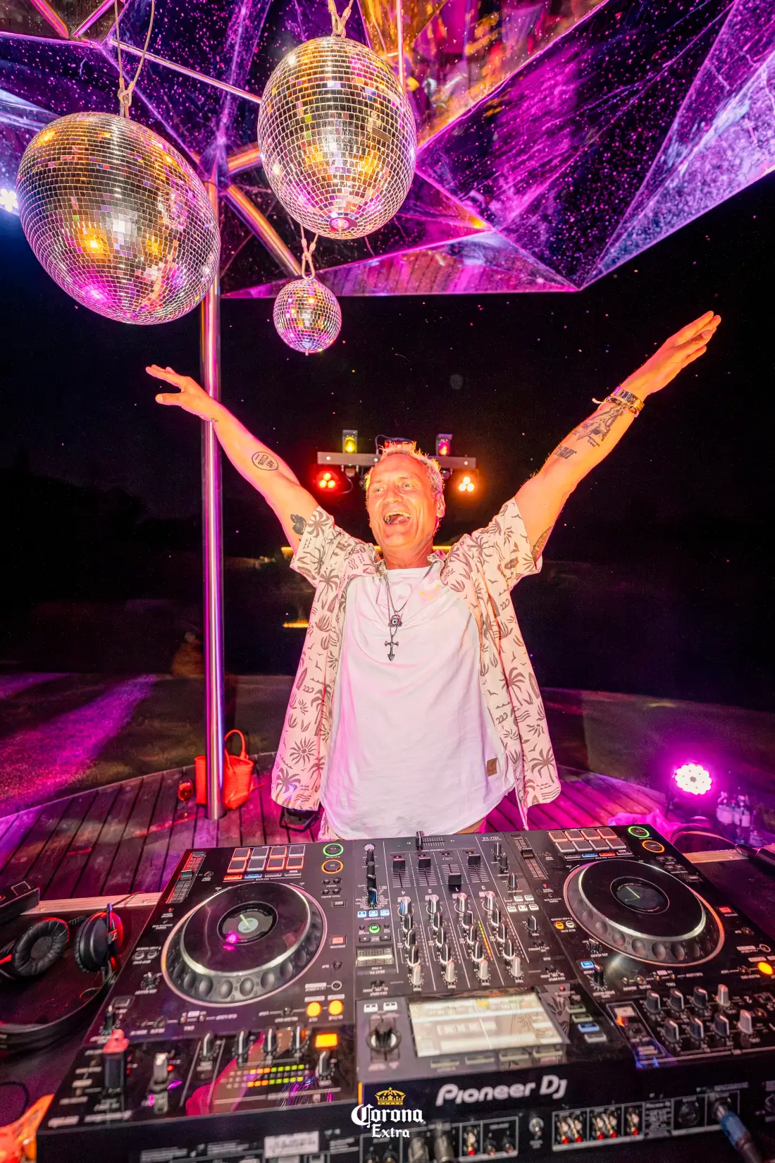 DJ with outstretched arms under disco balls at night