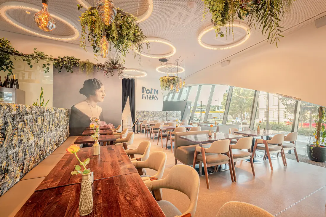 Café mit langem Holztisch, Ringleuchten und Pflanzen an der Decke