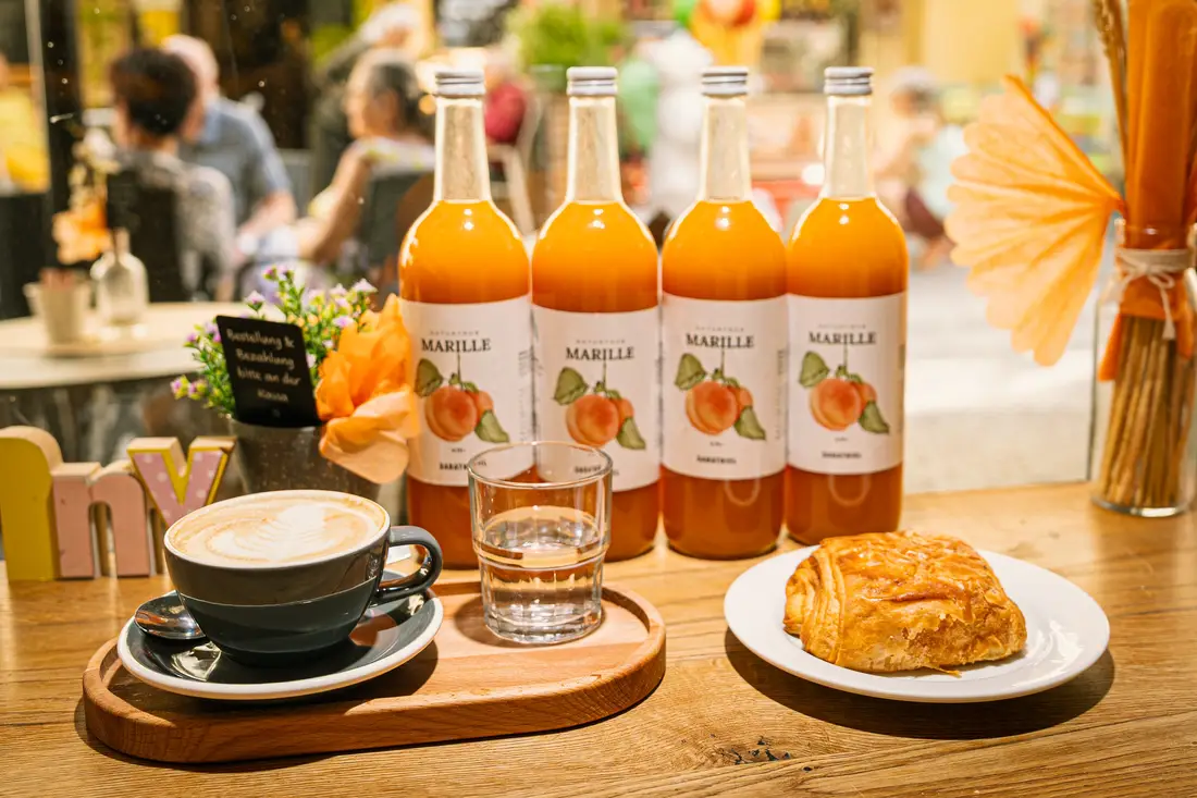 Marillensaft in Flaschen, Kaffee und Gebäck auf einem Cafétisch