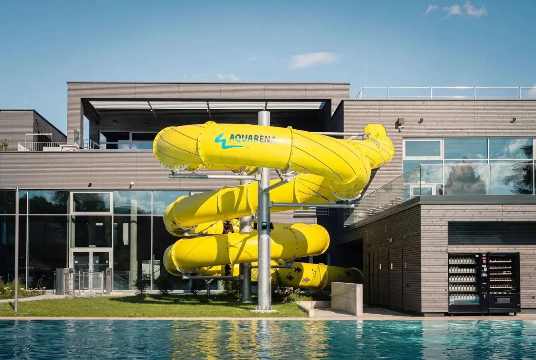 Yellow tube slide with the Aquarena logo in front of Bad Mirador, the outdoor pool in the foreground
