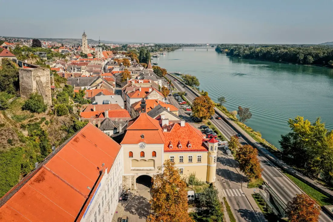 Luftaufnahme einer Altstadt mit roten Dächern direkt an der Donau
