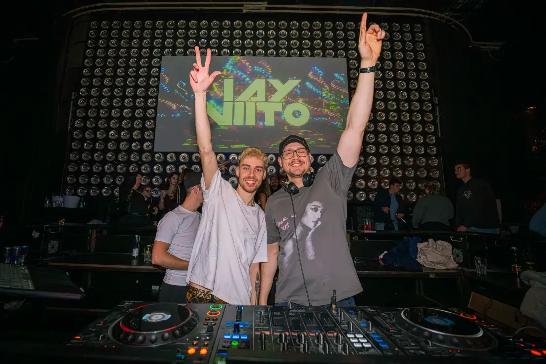 Two DJs cheering behind the mixing desk