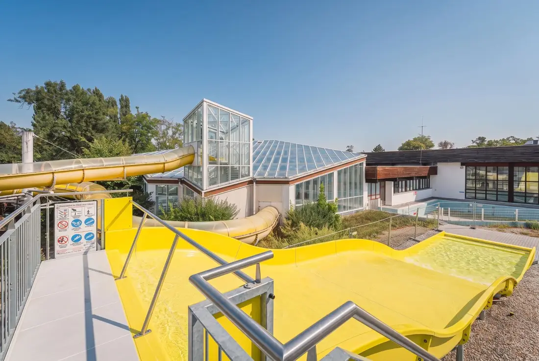 Yellow Aquarena wave slide at an outdoor pool with a glass tower and tube slide behind