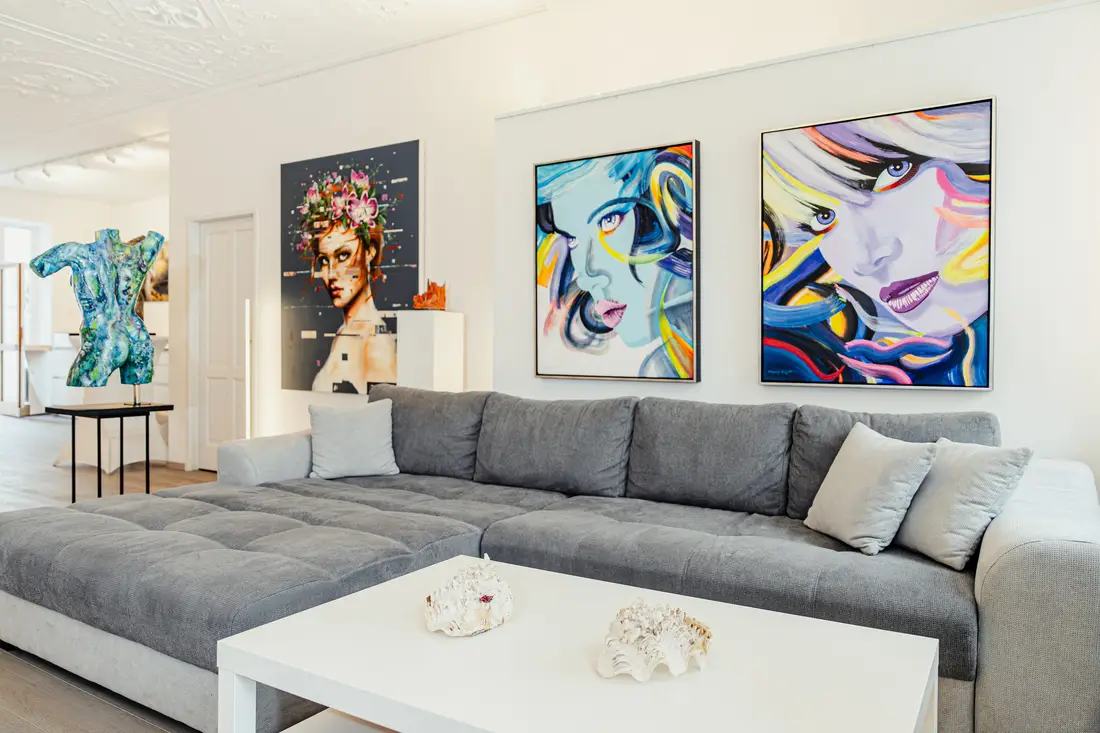 Wohnzimmer mit grauem Sofa und farbigen Porträtgemälden an der Wand