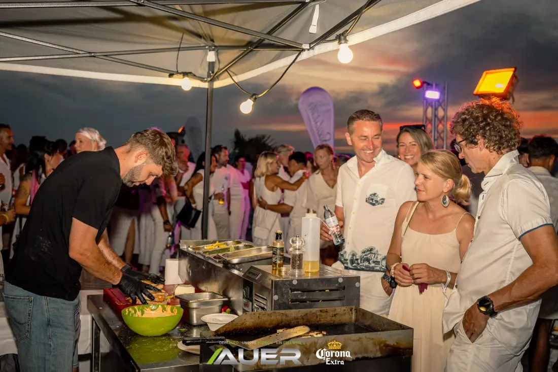 Chef preparing food, guests dressed in white beside him