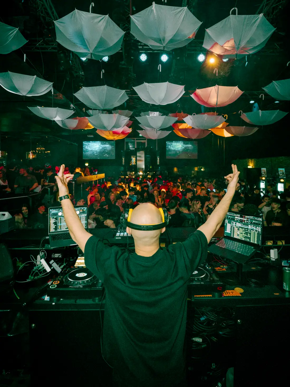 DJ seen from behind with raised arms, umbrellas hanging above the dance floor