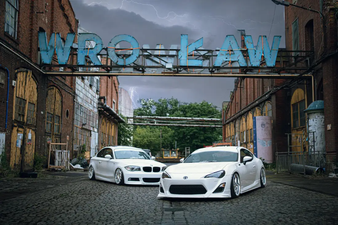 Zwei weiße tiefergelegte Autos in einem alten Industrieareal unter einem Wrocław-Schriftzug