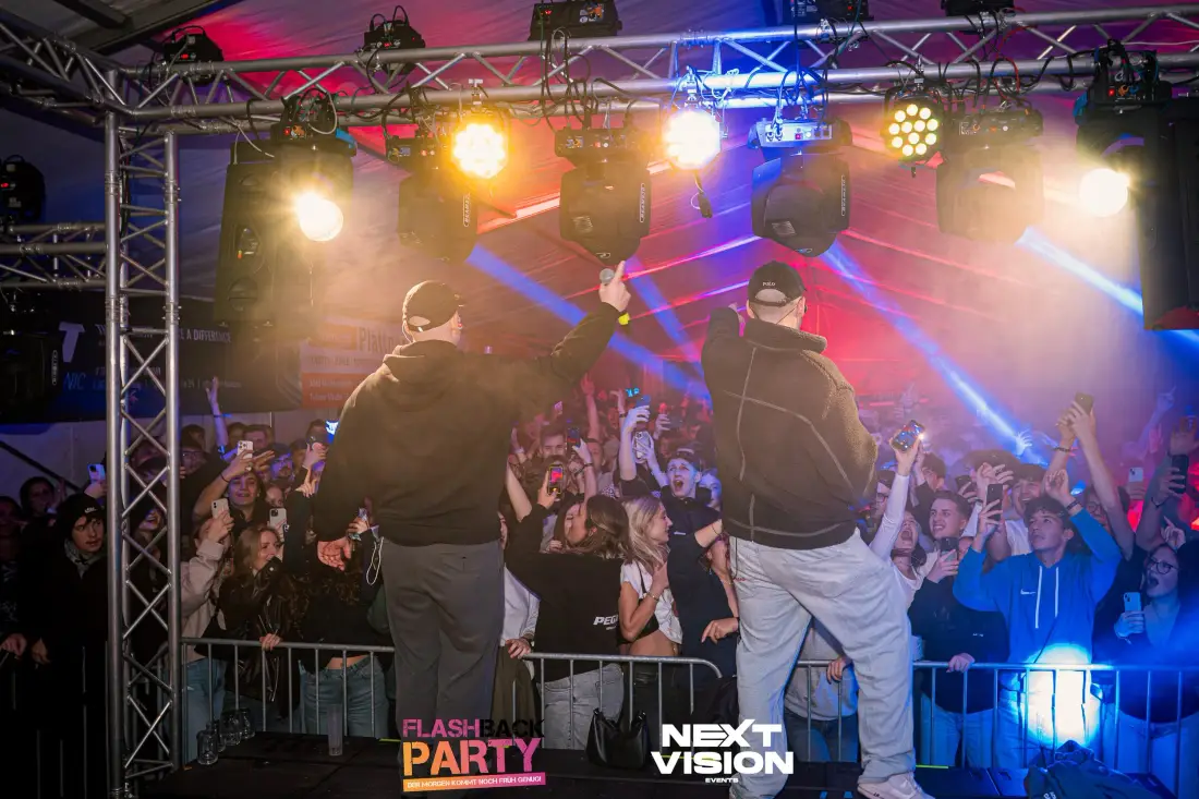 Two performers on stage in front of an audience behind barriers