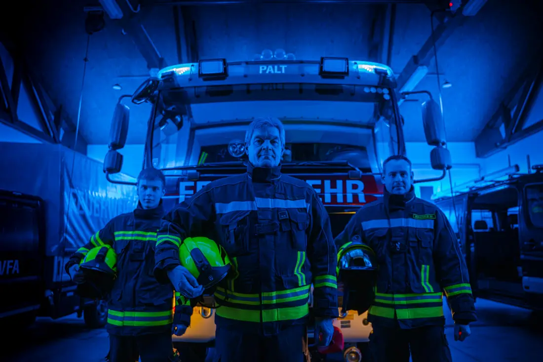 Drei Feuerwehrleute stehen im blauen Licht vor einem Löschfahrzeug der Feuerwehr Palt