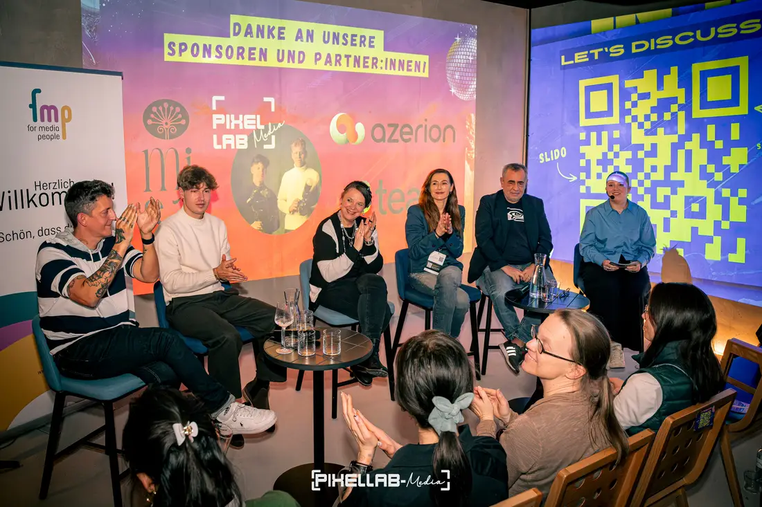 Podiumsdiskussion vor Publikum, auf der Leinwand dahinter Sponsorenlogos, darunter das von Pixellab-Media