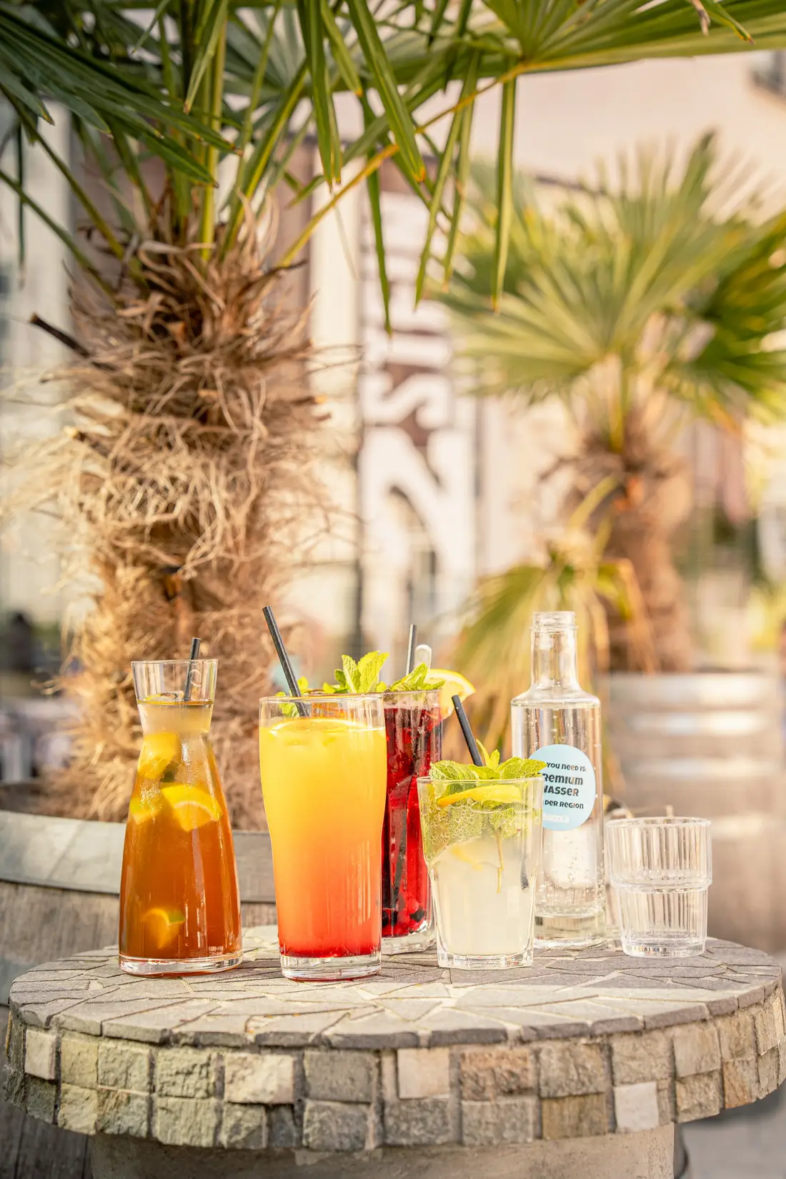 Bunte Sommergetränke auf einem Steintisch unter Palmen