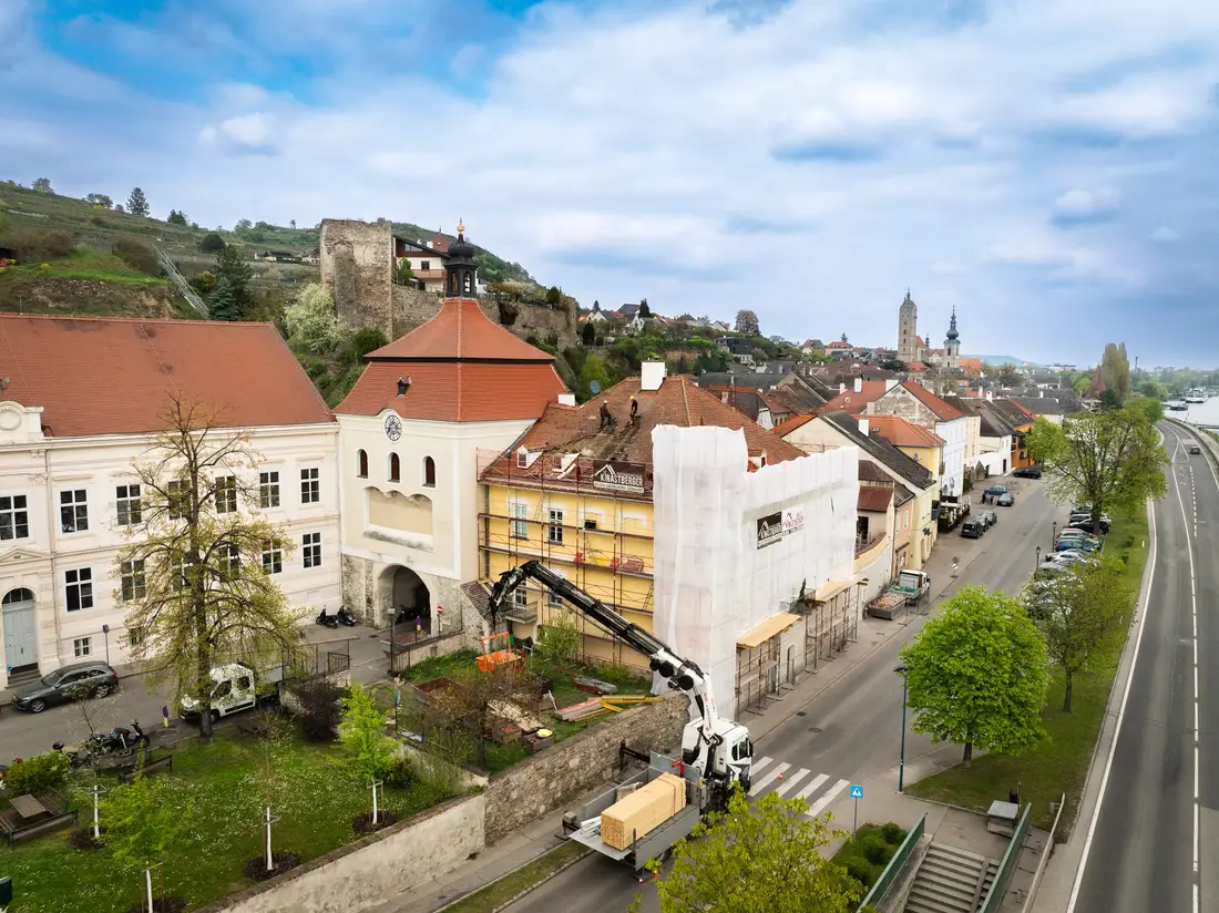 Luftaufnahme einer Baustelle in Krems-Stein: eingerüstetes Haus neben einem Torturm, ein Lkw-Kran hebt Material