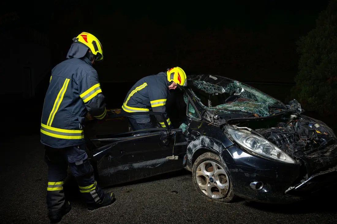 Zwei Feuerwehrleute arbeiten bei Nacht an einem zerstörten Auto