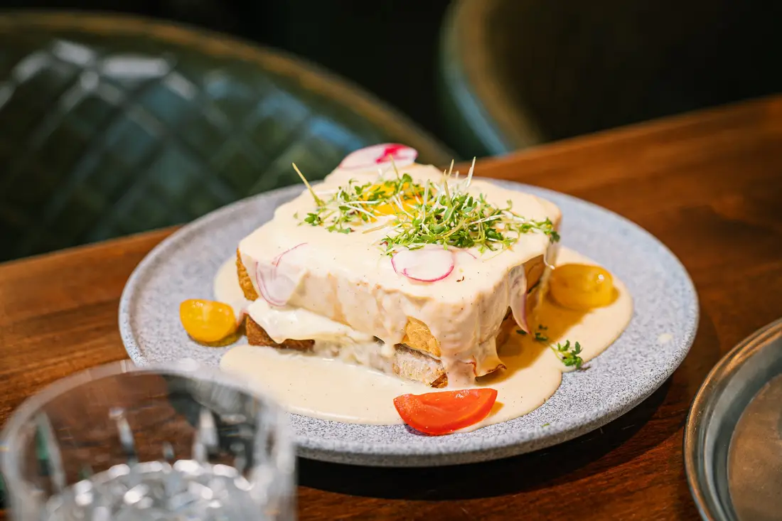 Überbackenes Sandwich mit heller Sauce, Kresse und Radieschen auf einem grauen Teller