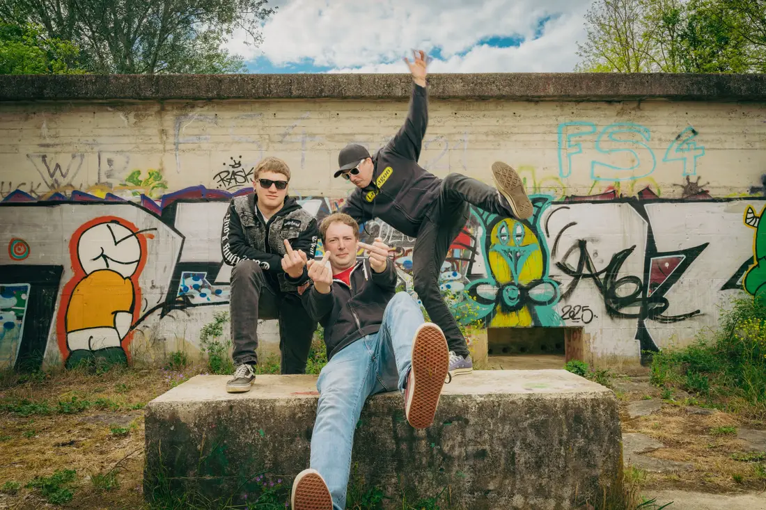 Drei junge Männer posieren vor einer Graffitiwand