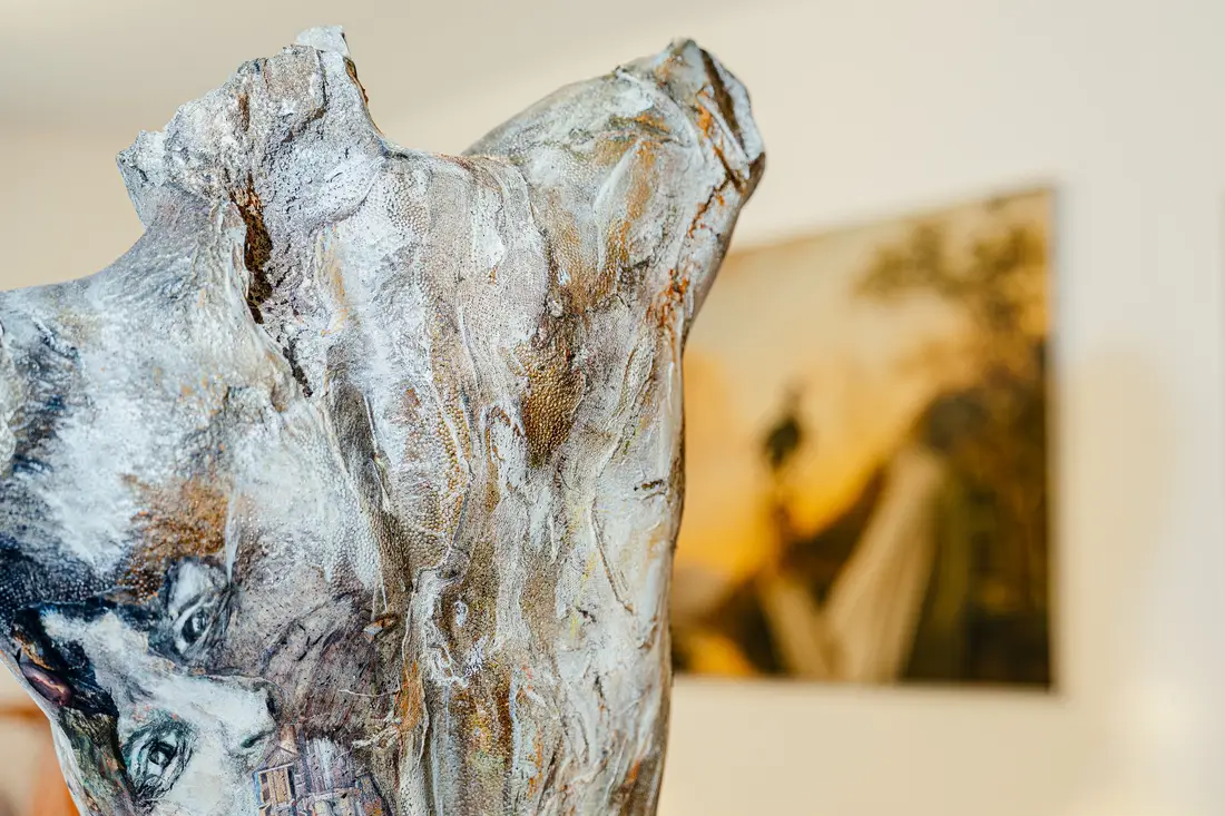 Nahaufnahme einer bemalten Torso-Skulptur, im Hintergrund unscharf ein Gemälde
