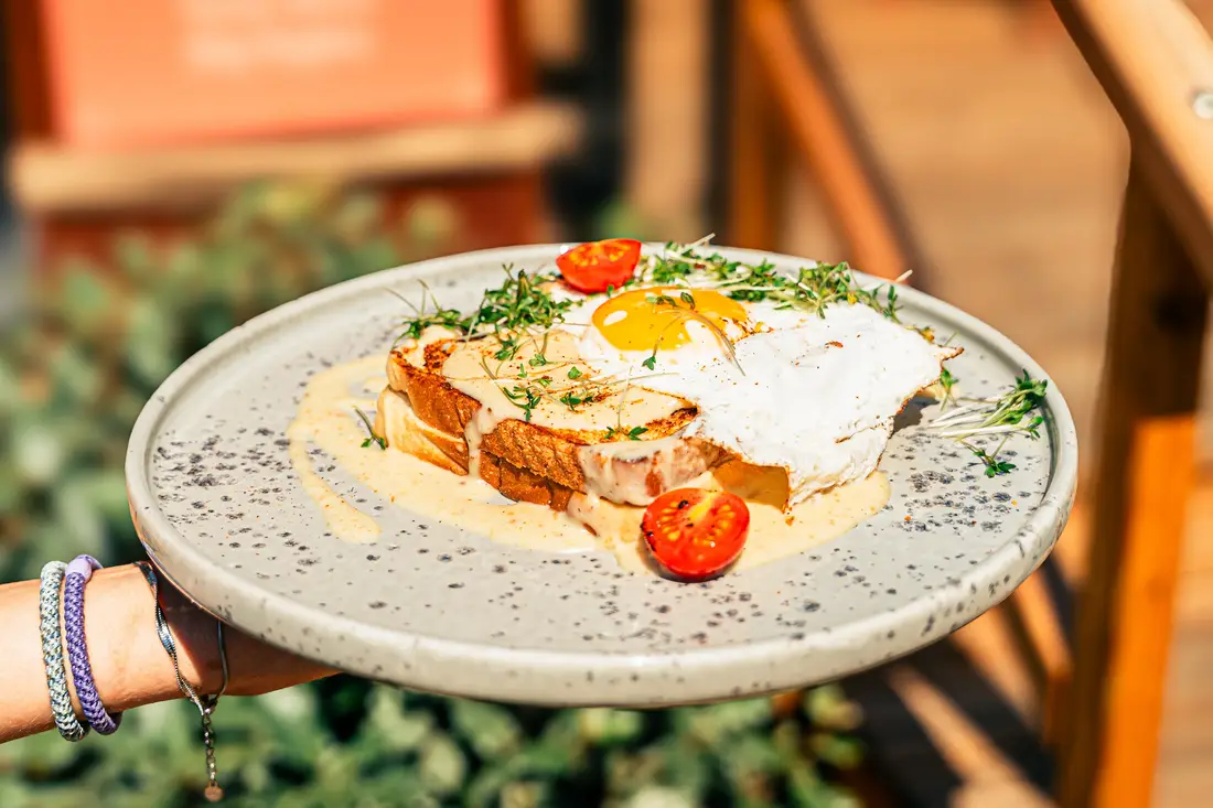 Toast mit Spiegelei, Sauce und Tomaten auf einem gesprenkelten Teller, von einer Hand gehalten
