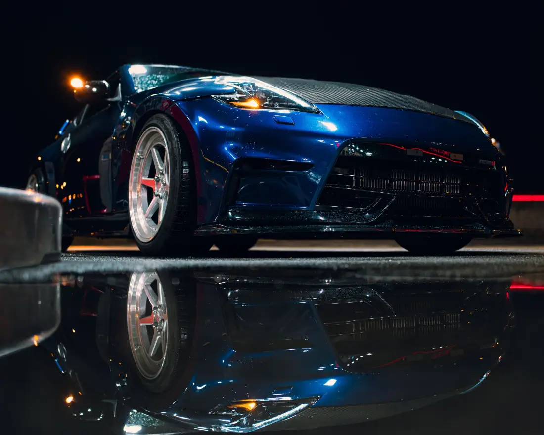 Blauer Sportwagen bei Nacht, gespiegelt in einer Wasserfläche