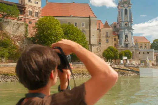 Over-the-shoulder view of a photographer shooting a church with a blue tower on the Danube
