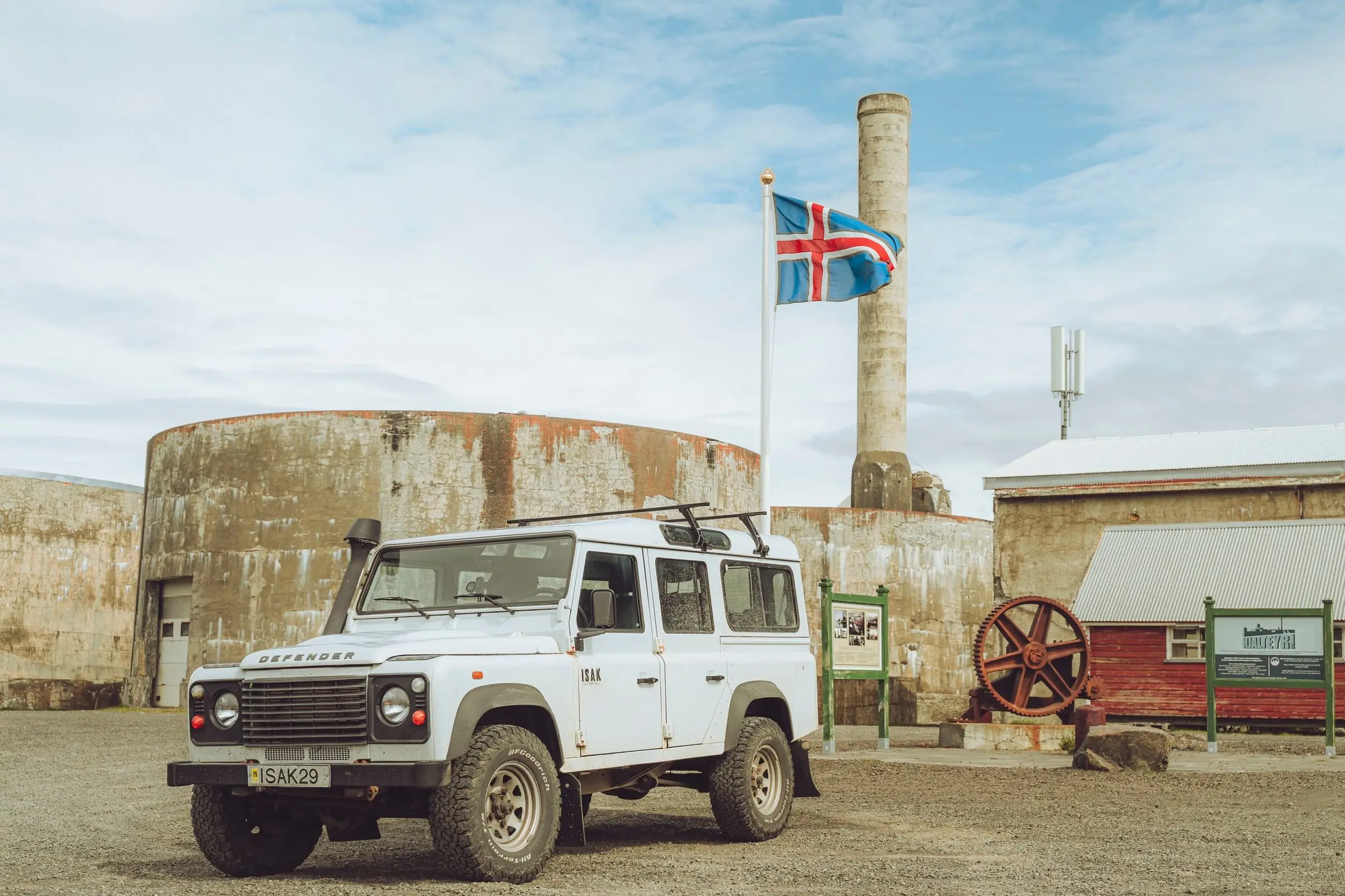 White Land Rover Defender in front of old factory buildings with an Icelandic flag