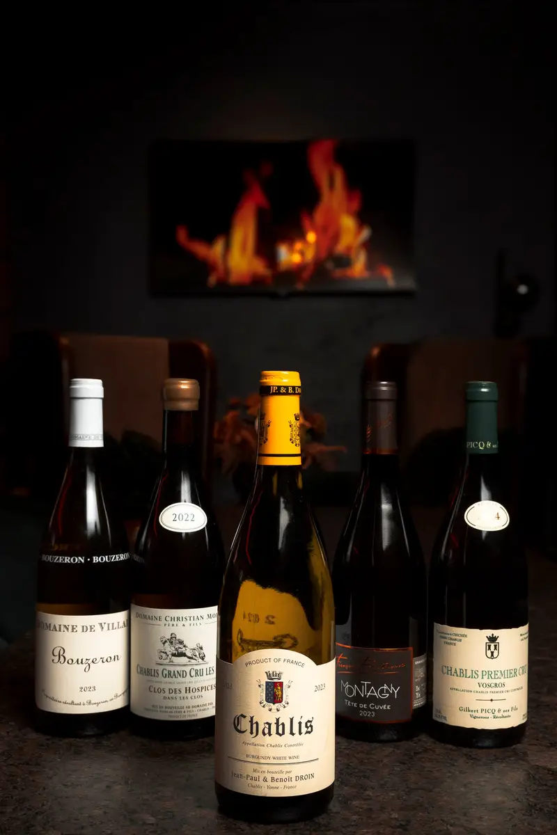 Wine bottles on a table, a bottle of Chablis in front, a fireplace behind
