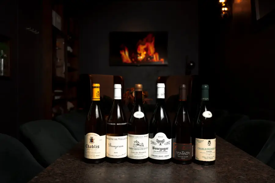 Six wine bottles side by side on a table, a fireplace behind