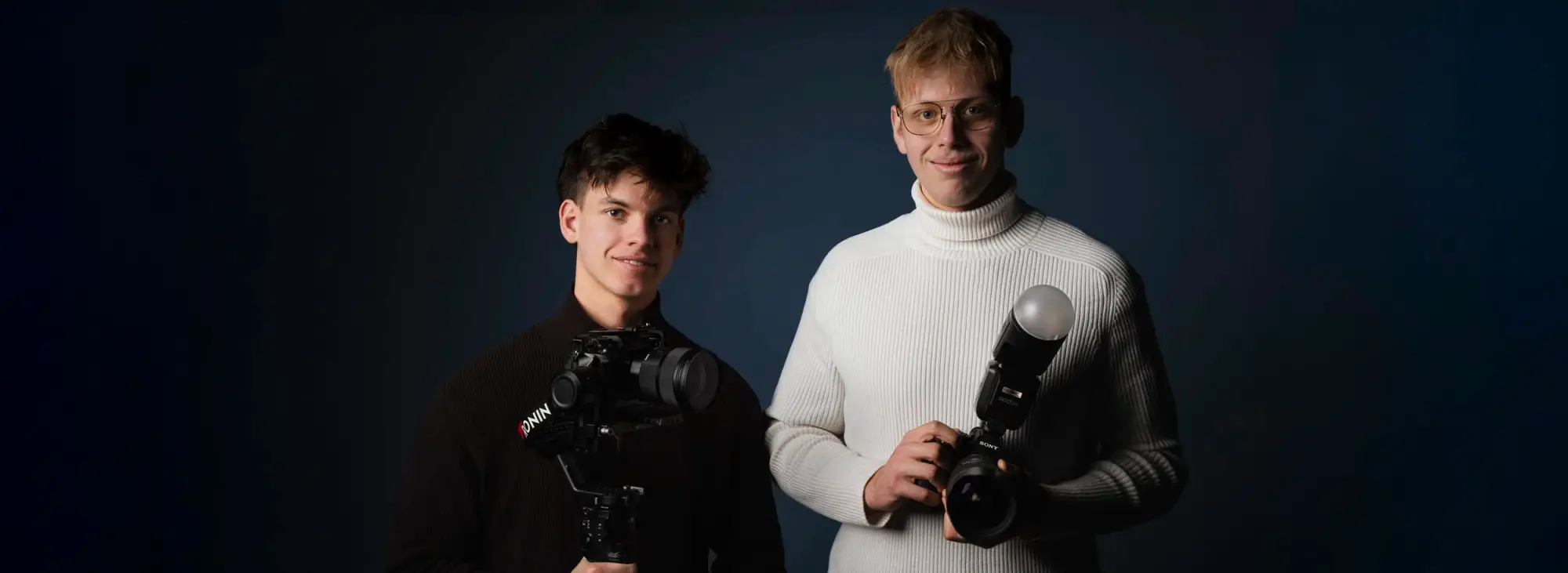 Paul Schneider and Bryan Schmied with cameras against a dark blue background